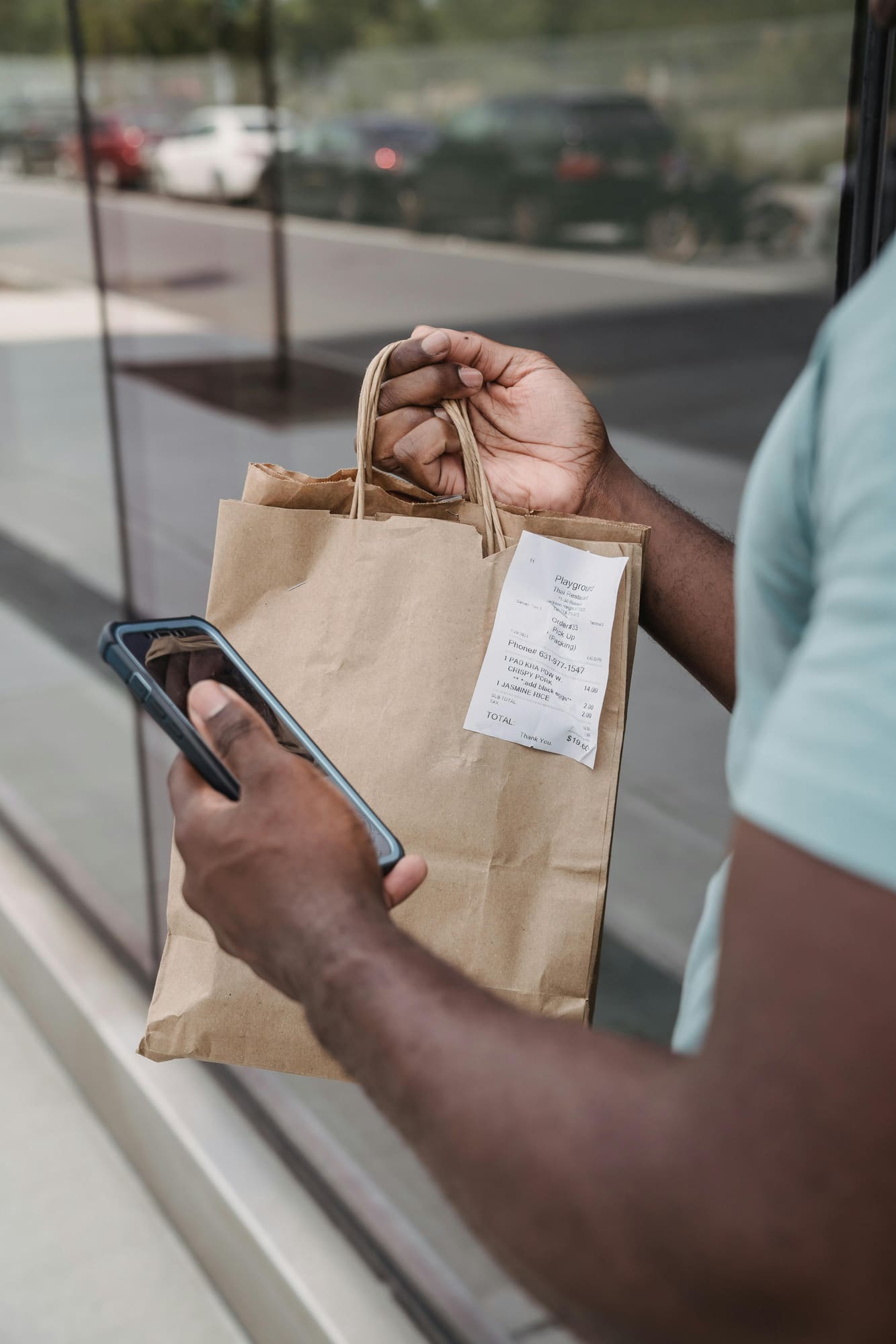 A hand holding a paper receipt next to a phone outside a shop